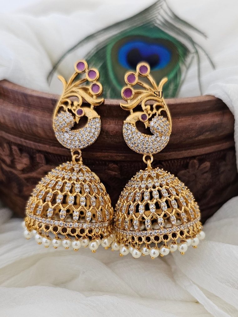 These exquisite peacock jhumkas boast a lavish gold finish, adorned with sparkling CZ and radiant ruby stones. Inspired by traditional elegance, they blend opulence with sophistication, perfect for adding a touch of glamour to any ensemble. Each intricately crafted piece exudes timeless beauty and unparalleled craftsmanship.