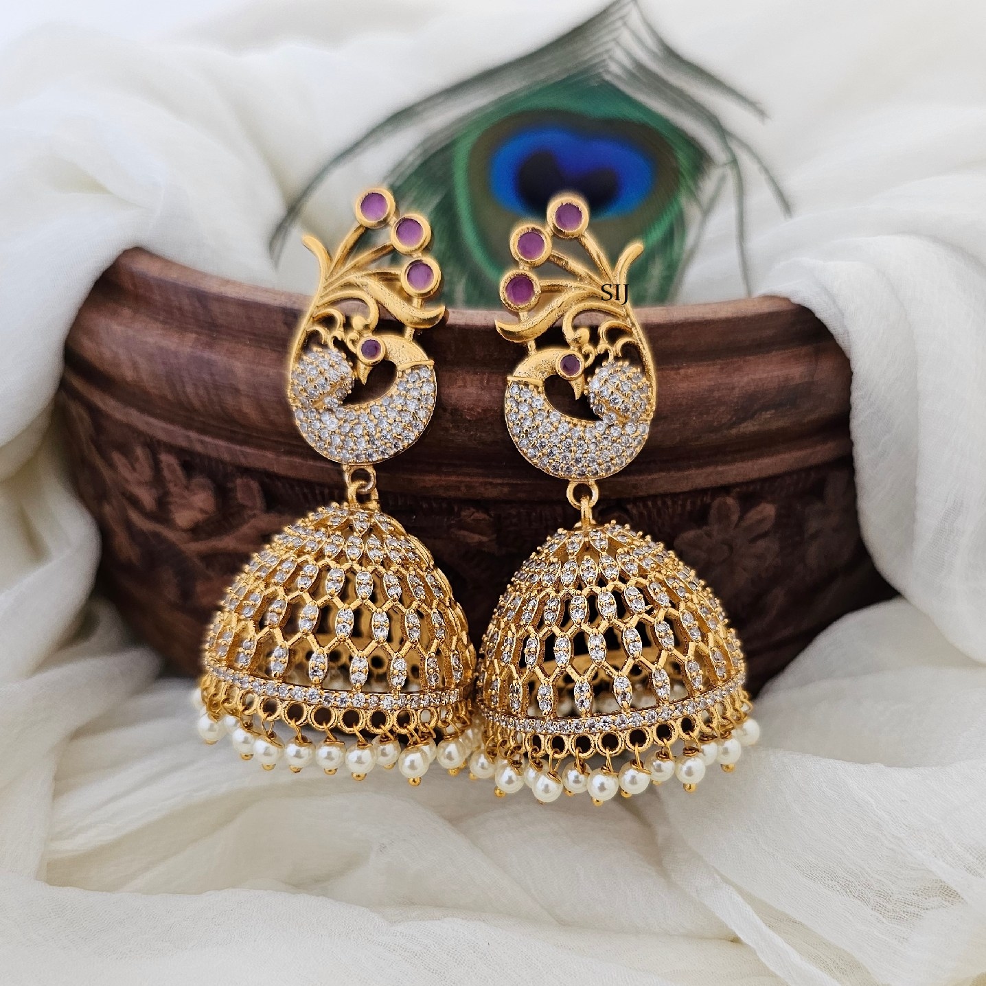 These exquisite peacock jhumkas boast a lavish gold finish, adorned with sparkling CZ and radiant ruby stones. Inspired by traditional elegance, they blend opulence with sophistication, perfect for adding a touch of glamour to any ensemble. Each intricately crafted piece exudes timeless beauty and unparalleled craftsmanship.